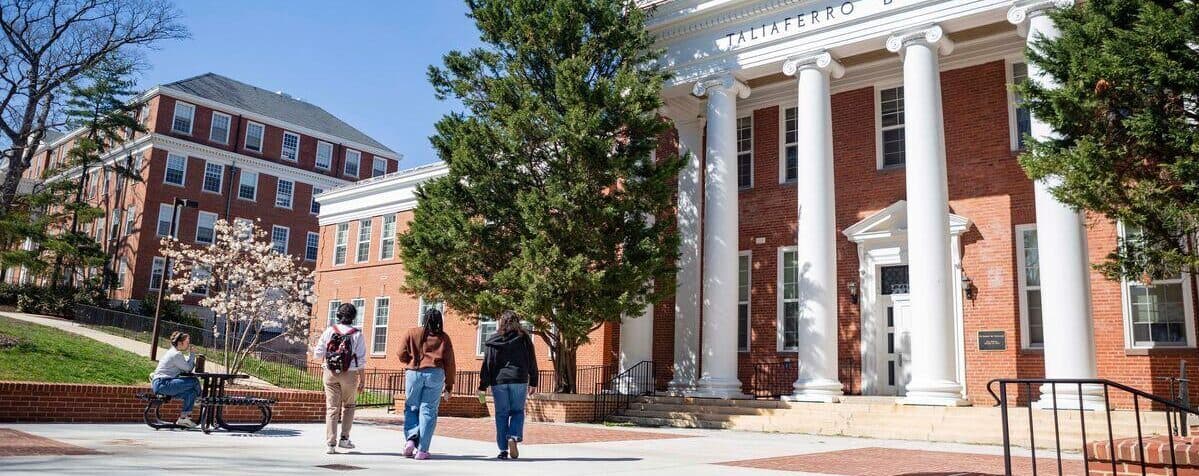 Students walking in front of Taliaferro Hall, a brick building with white columns.