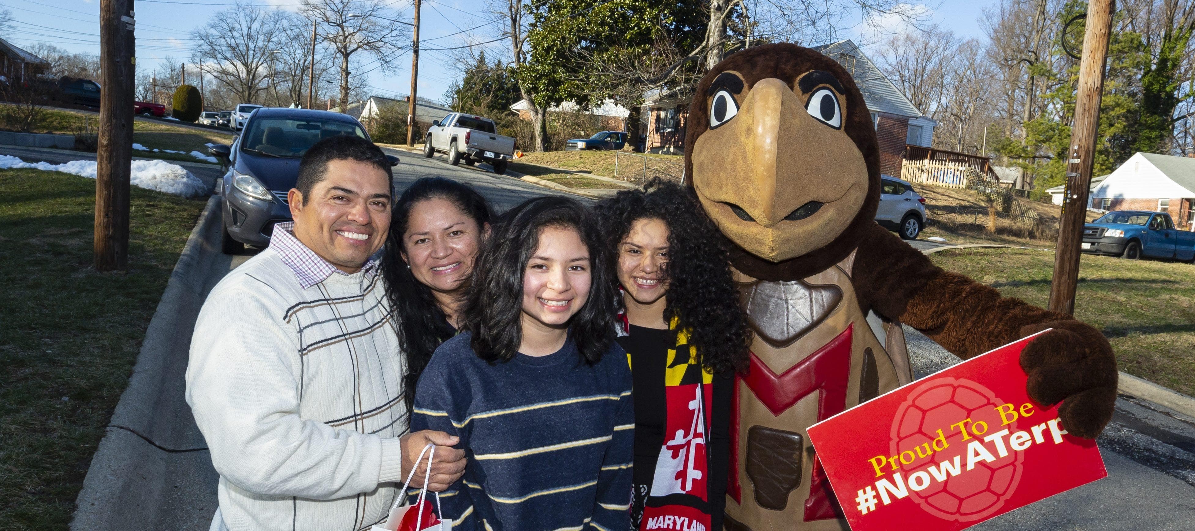 Family posing with Testudo, UMD's mascot and a sign that says "Proud to be #NowATerp".